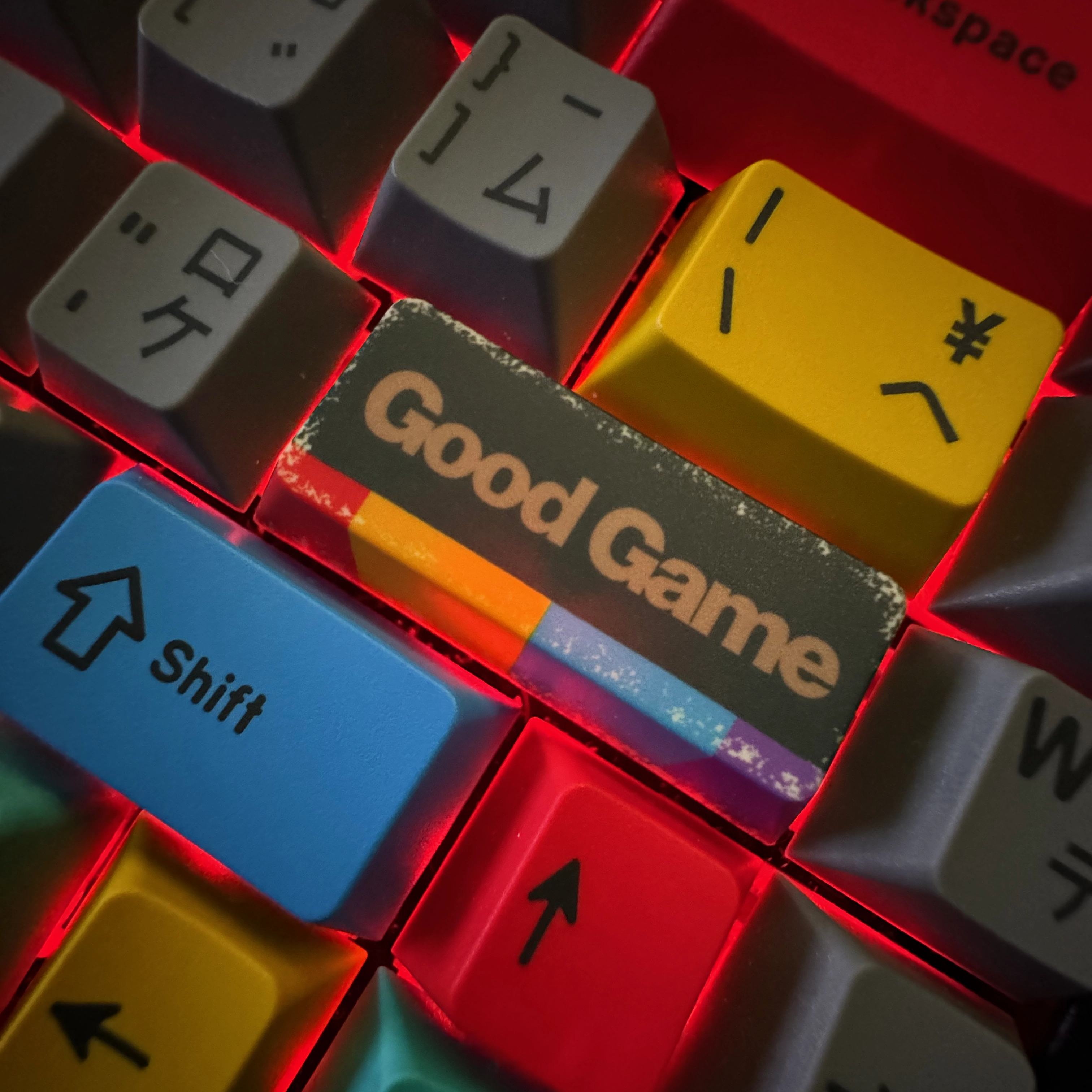 Closeup shot of a custom Enter key on a 75% keyboard. Instead of reading “Enter”, the key reads “Good Game”, which is what the cool hackers say once they ruin your digital identity. The keyboard is backlit in red, and the Enter key is surrounded by other multicolored keys with both English and Japanese (Katakana) symbols.